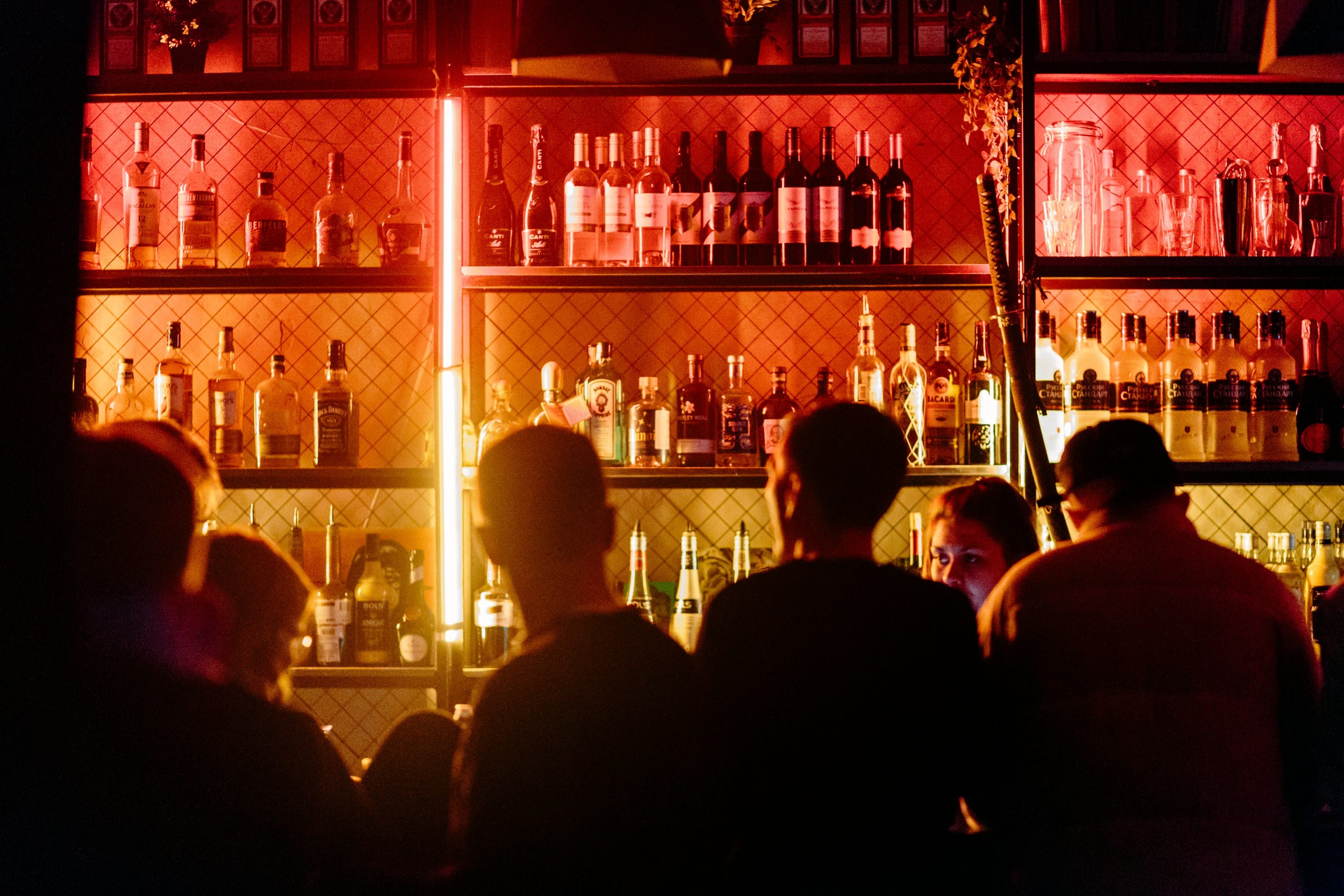 Guests at a dimly lit bar with a back-lit spirits shelf